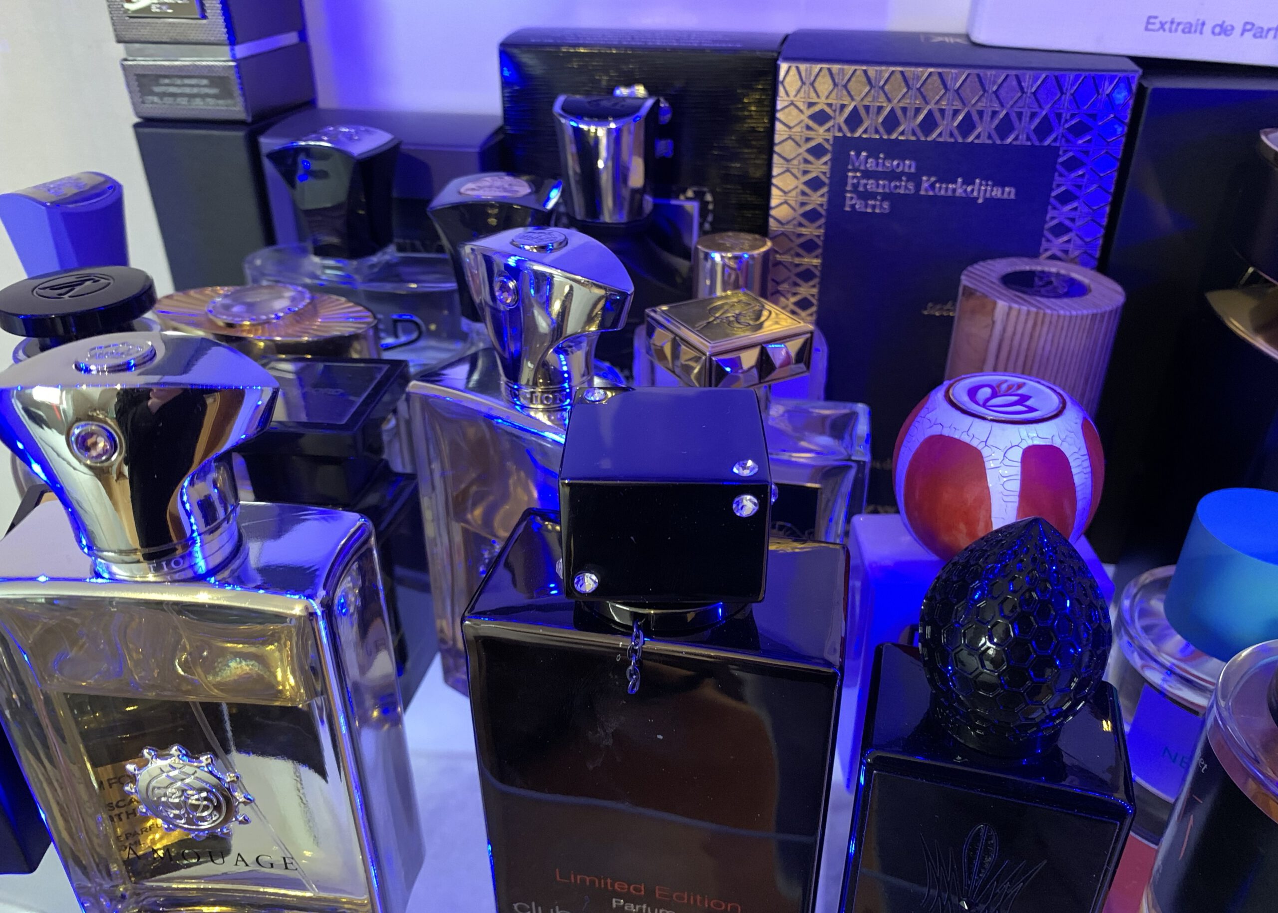 Viele verschiedene Parfümflakons mit unterschiedlichen Deckeln, in bläuliches Licht getaucht. Im Hintergrund die Verpackung einiger Duftfläschchen.